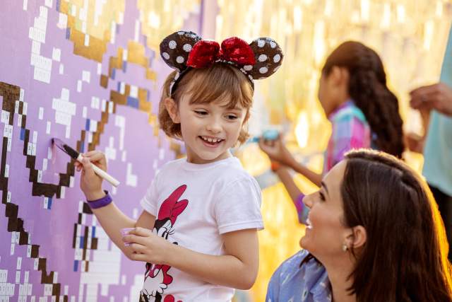 A young girl painting while her mom watches at the Epcot® 2023 Festival of the Arts