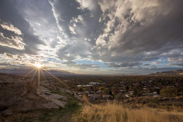 View of the Salt Lake Valley from the south with the sun shining.  Grass and boulder in the foreground, mountains in the background