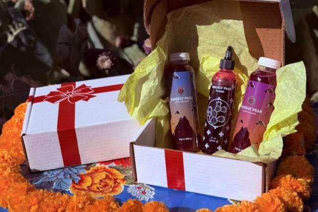 Two gift boxes containing colorful bottled products, set among vibrant orange flowers and cacti.