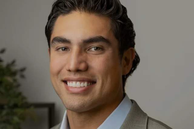 Smiling man in medium grey blazer and light blue button up shirt