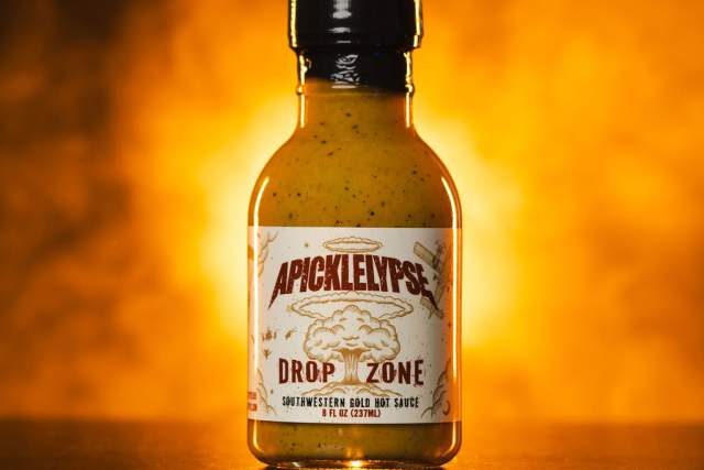 A bottle of "Apickelypse Drop Zone" Southwestern Bold BBQ Sauce against a fiery backdrop.
