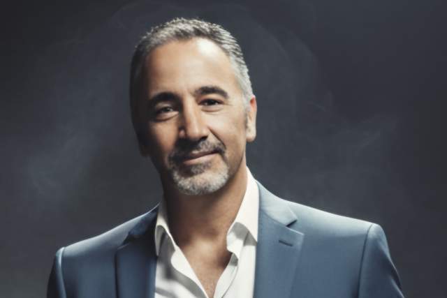 Half smiling man in dark grey suit with white button up shirt