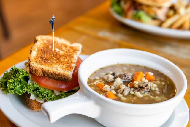 Aerial view of two plates of food. One plate has a burger and fries on it while the other has a half a sandwich and soup.