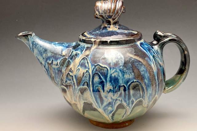 Ceramic teapot with a blue and grey drip glaze finish, featuring a curved spout and a decorative handle.