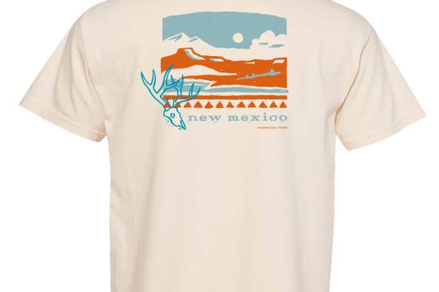 A t-shirt featuring a stylized landscape graphic on the back. The design includes mountains, a prominent sun, a deer, and the text "New Mexico" with "Georgia's View" below.