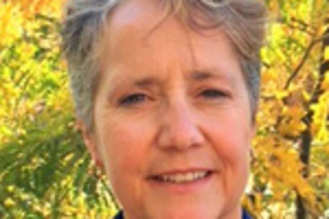 Smiling woman in blue suit coat and dark pink shirt standing in front of golden aspens