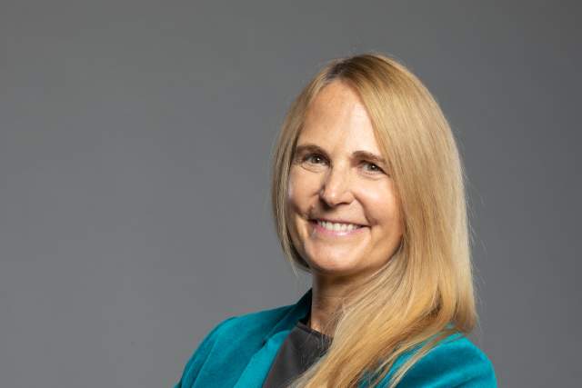 Smiling woman in teal suit coat with her arms crossed