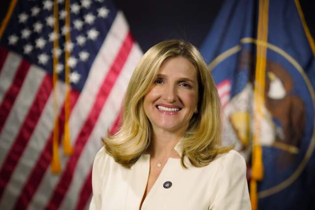 Smiling woman in cream dress sitting in front of the US and Utah state flags