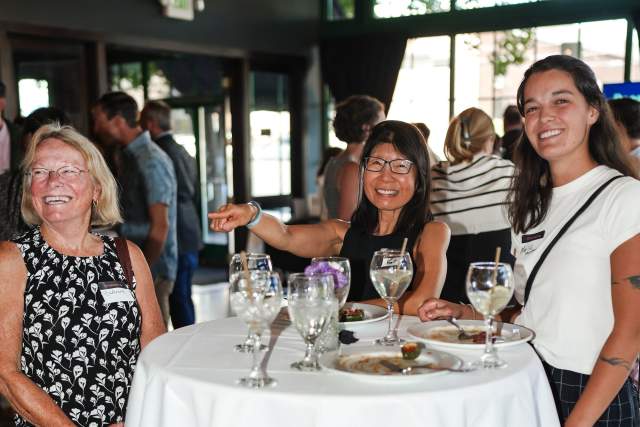 Three women standing at a tall table smiling and engaging