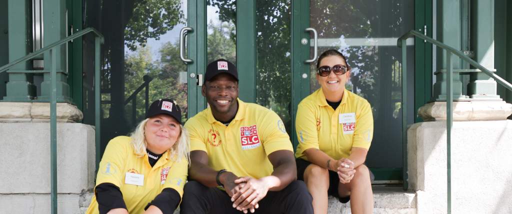 Three people sitting on steps wearing yellow downtown ambassadors shirts