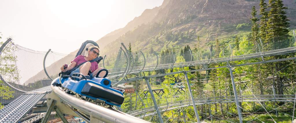 Woman looking like she is going fast around a corner on a single person coaster with sky and mountains around her