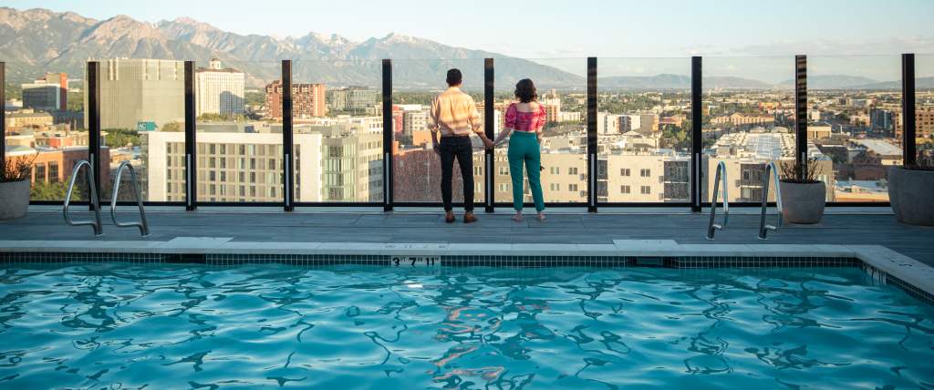 View of downtown Salt Lake looking across a pool with 2 people standing near the edge overlooking the city