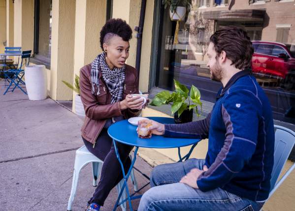 A woman and man sip coffees at a table in front of Cured. On Columbia in downtown Covington.