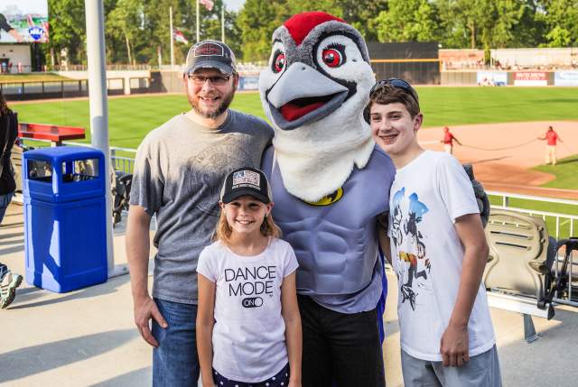 Family posing with a baseball team mascot at a stadium, smiling during a game-day event