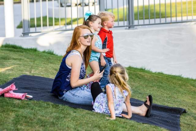 Family relaxing on a blanket outdoors with children sitting on the grass at a community event