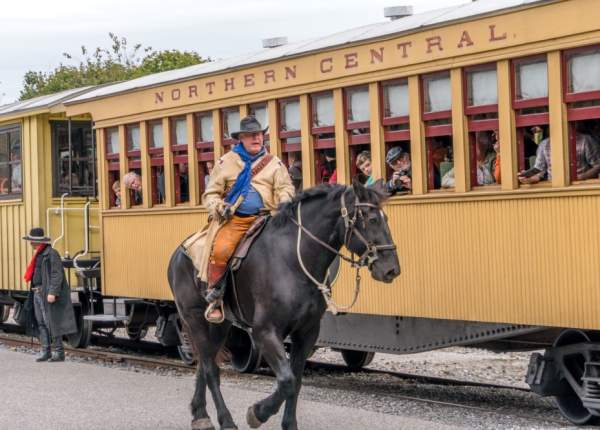 cowboy riding a horse next to a northern central railway train