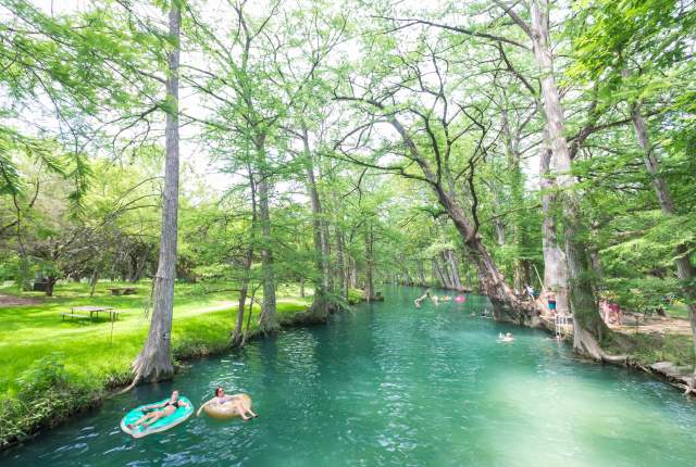 People floating on Blue Hole in pink and blue innertubes, with trees lining the shoreline.