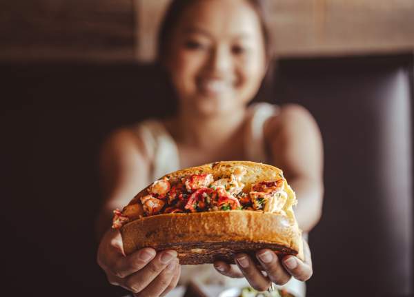 a very happy girl holding up a lobster roll at Rockfish Public House
