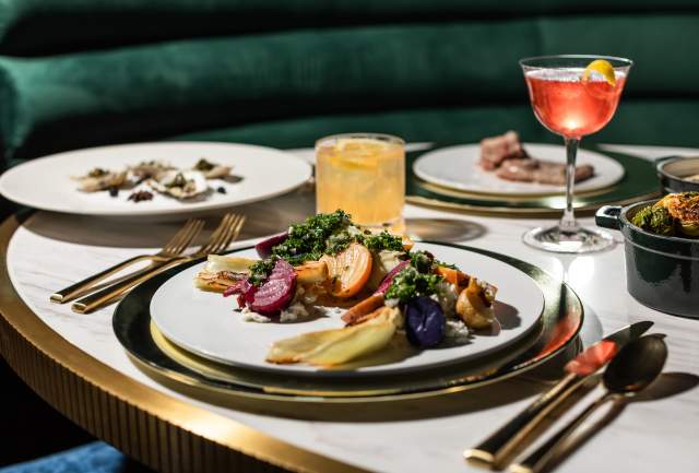 A table is set with multiple plates of brightly colored vegetables and a pink cocktail