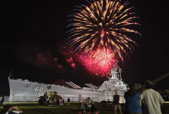 Red fireworks explode at night above the USS ALABAMA battleship