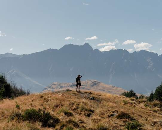 Person at the top of the Queenstown Hill summit with mountains behind them