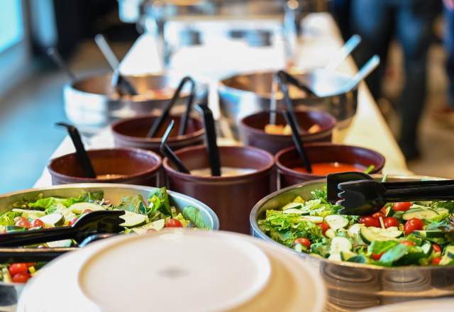 A beauty shot of a buffet table, prominently featuring a colorful garden salad in focus in the foreground, along with dressing bowls and other dish bowls slowing becoming more out of focus the further up in the photo.