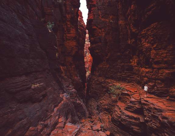Woman walking through Knox Gorge in Karijini National Park, with towering red rock gorge walls