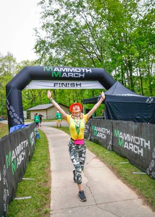 A woman celebrates with her hands in the air at the finish line of MammothMarch at Oak Mountain State Park.