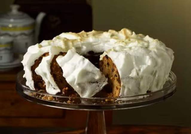 a cake sitting on top of a glass mount with white icing and plates and forks beside it