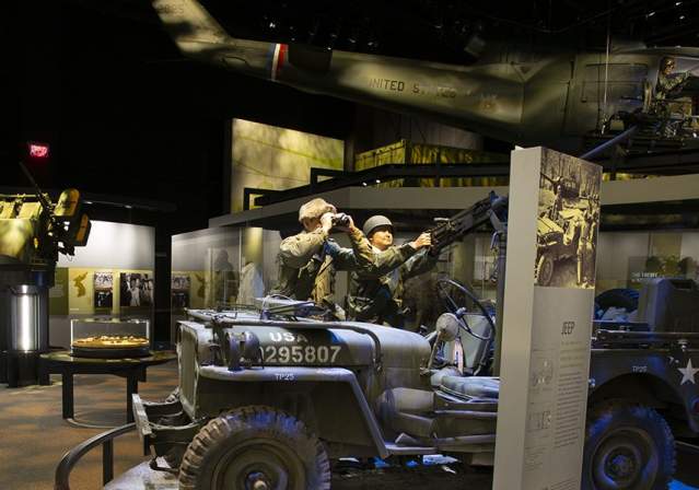 Huey helicopter hanging from ceiling and Army jeep with soldiers in a room surrounded by Vietnam war information and soldier profiles