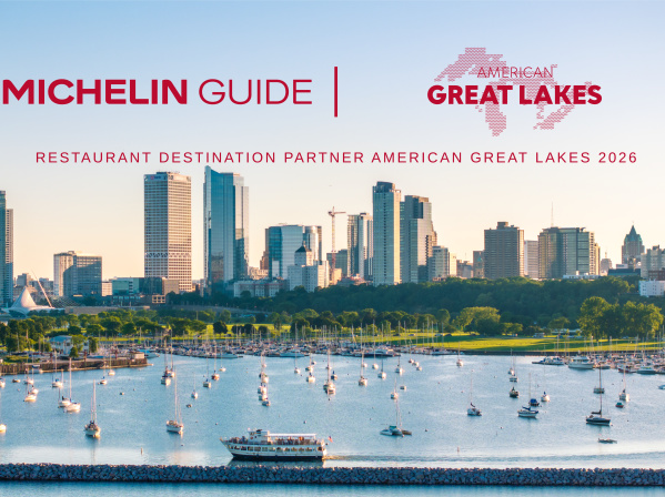 A waterfront view of Milwaukee’s skyline at sunset, with sailboats docked in the marina and a tour boat moving across Lake Michigan in the foreground. Above the skyline, red text reads “Michelin Guide | American Great Lakes” with the subheading “Restaurant Destination Partner American Great Lakes 2026.”