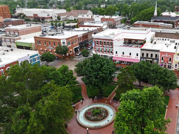 Bird's eye view of the Bentonville square, featuring a circular fountain surrounded by lush trees, and the city's historic main street in the background.