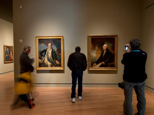 Visitors explore an art gallery featuring portraits of President George Washington in ornate frames.