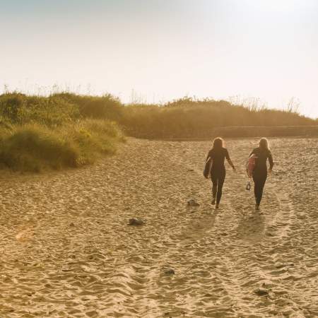 Two ladies walking across the beach with surfboards