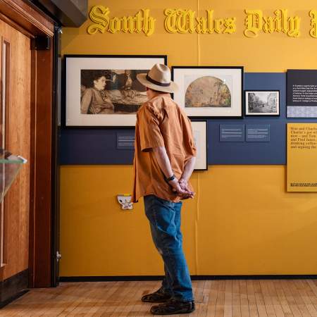 A man looking at picture in an exhibition on a yellow wall.