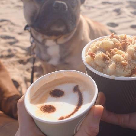 couple and their dog sitting on the beach with coffees