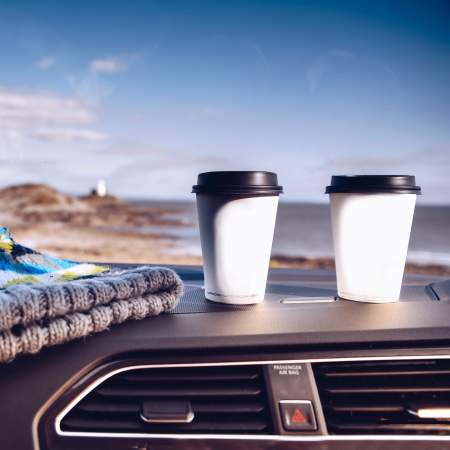 two coffee cups and a bobblehat on a car dashboard