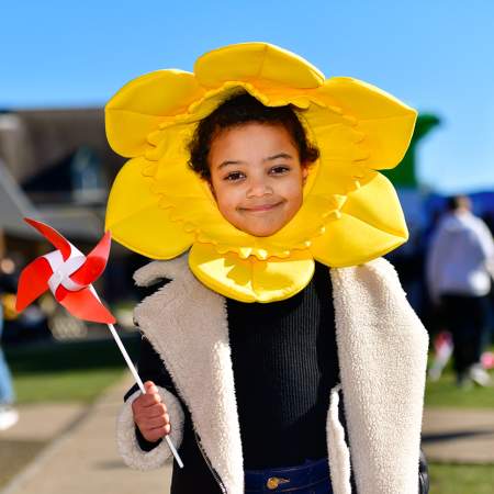 A child wearing a daffodil head dress, holding a windmill.