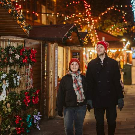 Young couple holding hands and exploring Swansea Christmas Market at night