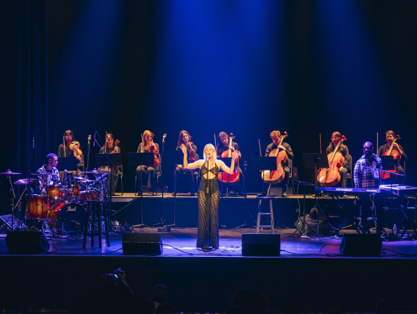 Grace Weber singing at a stand up mic with a string octet behind her