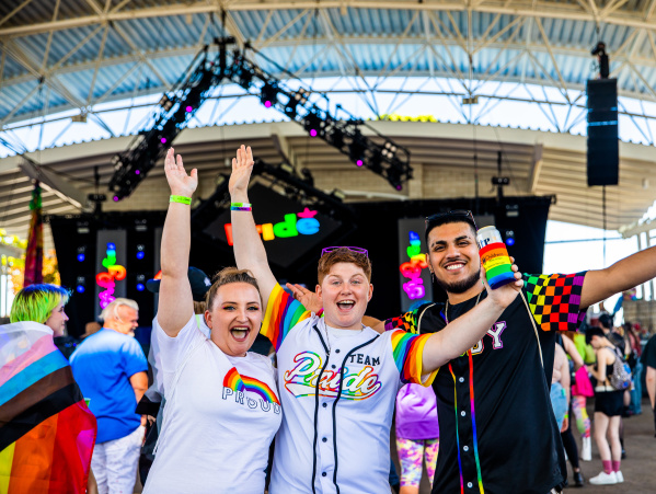 three friends cheering in front of a stage at pridefest