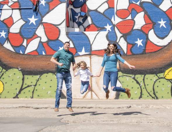 A family of three jumping for a picture in front of a texas butterfly mural in downtown amarillo