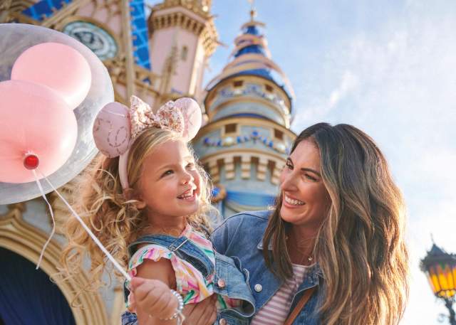 Mother and daughter holding a balloon in front of the castle at Magic Kingdom® Park