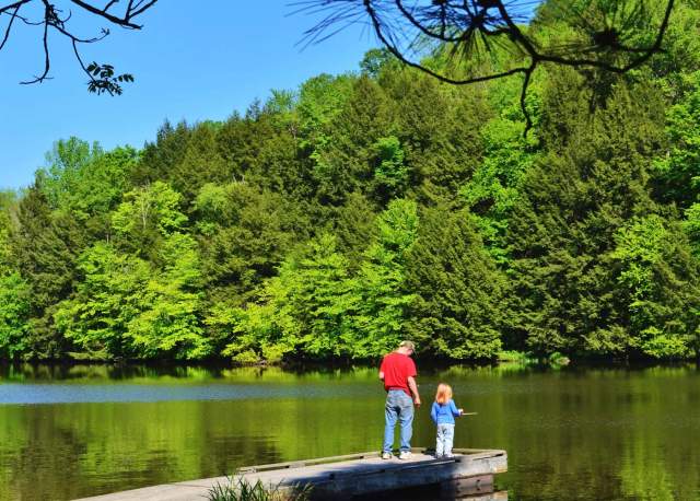 Man and a young girl standing on a dock fishing on a lake