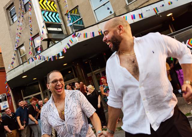 Two men hold hands while walking across a street. In the backgroud is a crowd lined up outside of the club, Karma in Harrisburg.