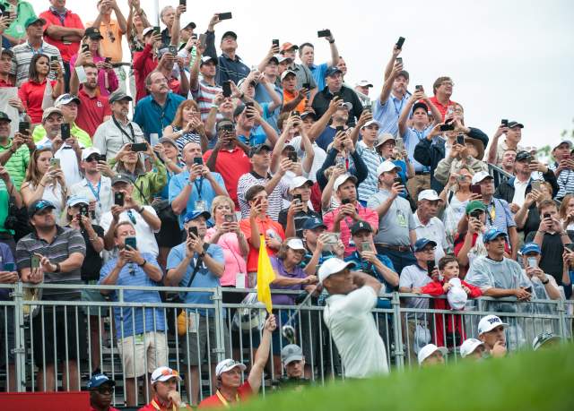 People in stand watching a person hit a golf ball with a club