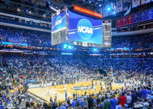 View of men playing a basketball game in Xfinity Mobile Arena with fans in the stands.