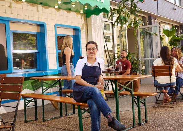 A woman sits on a picnic table outside Duo's Taqueria in Pittsburgh with people dining in the background.