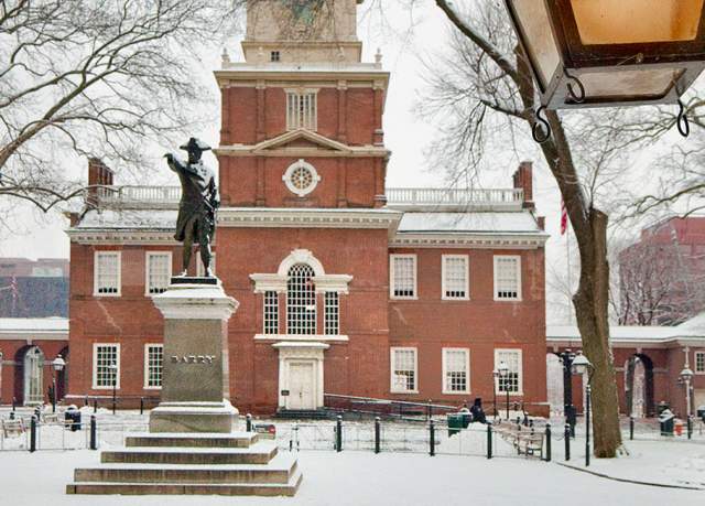 Independence Hall in Philadelphia with a statue in front of it and snow covering the ground