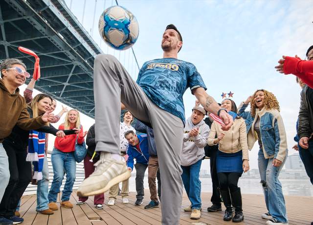 A man playing with a soccer ball with people cheering and standing around him